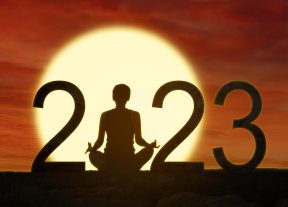 Silhouette of young woman practicing yoga while sitting with 2023 numbers in dawn sky background
